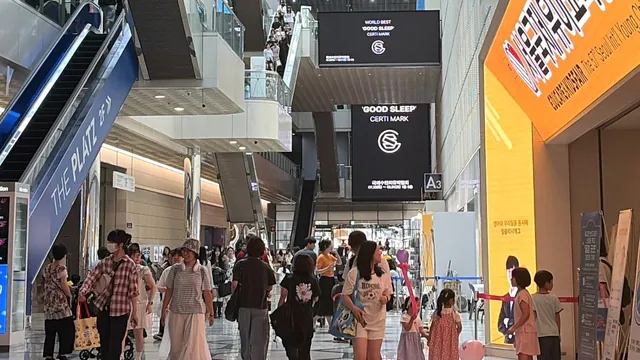 코엑스 로비의 굿슬립 인증마크 전광판과 관람객